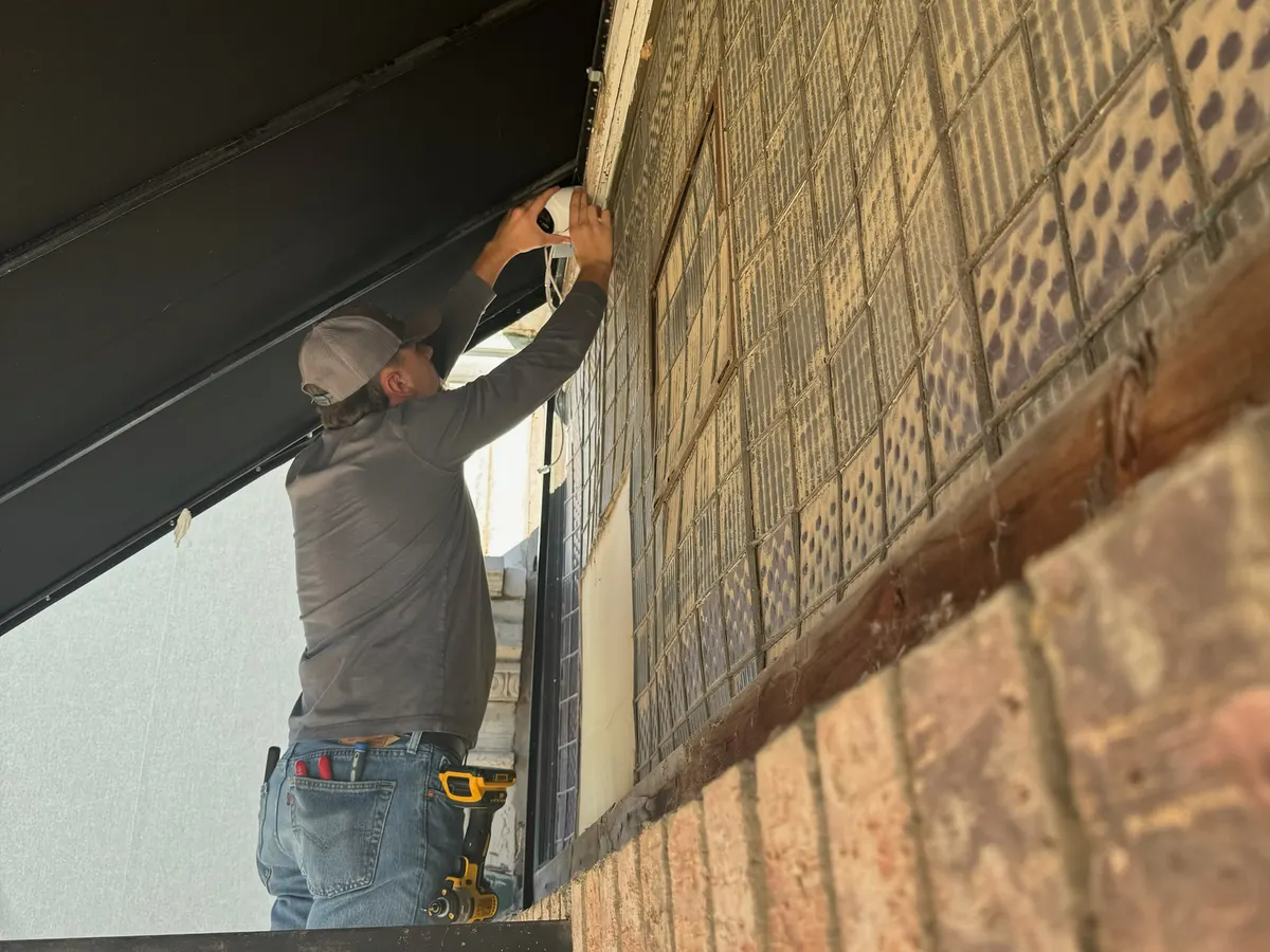 Technician mounting a camera under the eave of a brick building